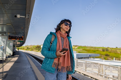 A young woman stands on the platform waiting for a train. A girl at the station.