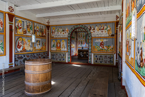 View of the interior of a reconstructed wooden church at Ribe VikingeCenter featuring colorful religious wall paintings, a wooden baptismal font, and wooden benches in Ribe, Jutland, Denmark.