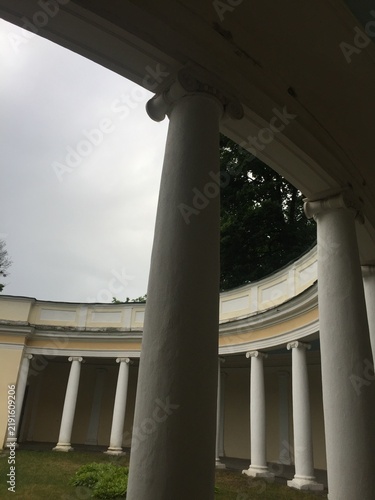 Bild auf Leinwand Classical rotunda architecture with white round stone columns, curved yellow walls, and a colonnade under an overcast sky