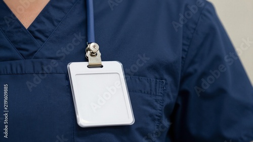 Close-up of a blank medical ID badge clipped to blue scrubs worn by a healthcare professional.