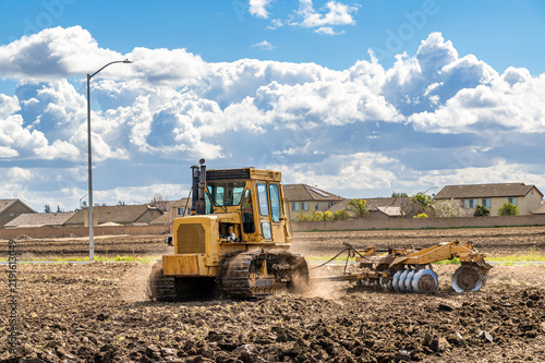 Bulldozer tilling soil with disc harrow near residential neighborhood. Agricultural machinery.