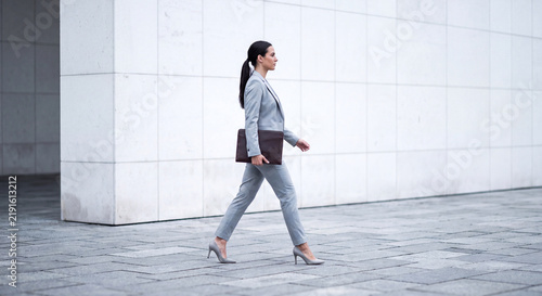 Professional woman in a grey suit walking confidently outdoors near a modern white building