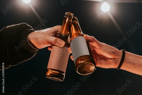 Obraz na płótnie Hands clinking beer bottles under bright stage lights