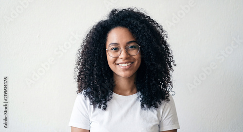 Portrait of a smiling young woman with curly hair and glasses isolated on white background