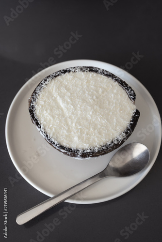 Creamy coconut ice cream served in natural coconut shell, topped with shredded coconut on white plate with spoon. Trendy dessert