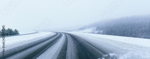 Snowy highway curving through a misty winter landscape with snow covered trees and overcast sky