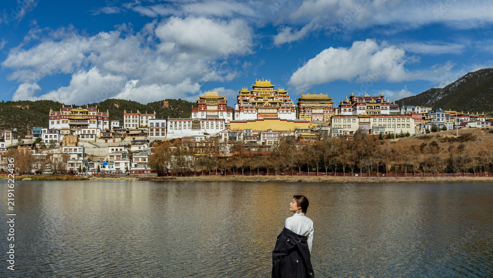 Fototapeta premium Woman gazing at Songzanlin Monastery reflected in the lake, wide view