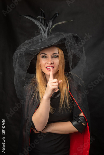 Cuadro en lienzo Woman witch wearing a black costume with hat and cape, making a shushing gesture