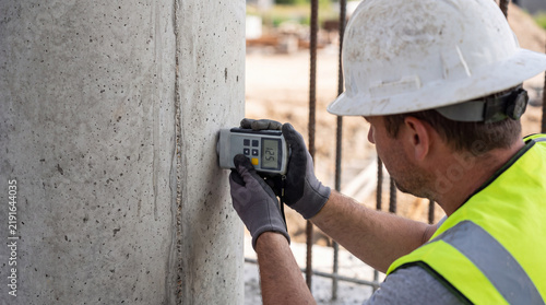 Construction professional inspecting concrete pillar with digital measuring device on urban worksite