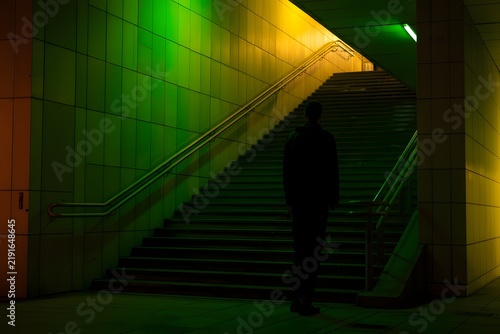 Urban staircase ascent with a solitary figure under dramatic green and yellow light