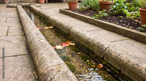 Water feature rill with autumn leaves in a tranquil stone patio garden, flowing channel for backyard landscaping