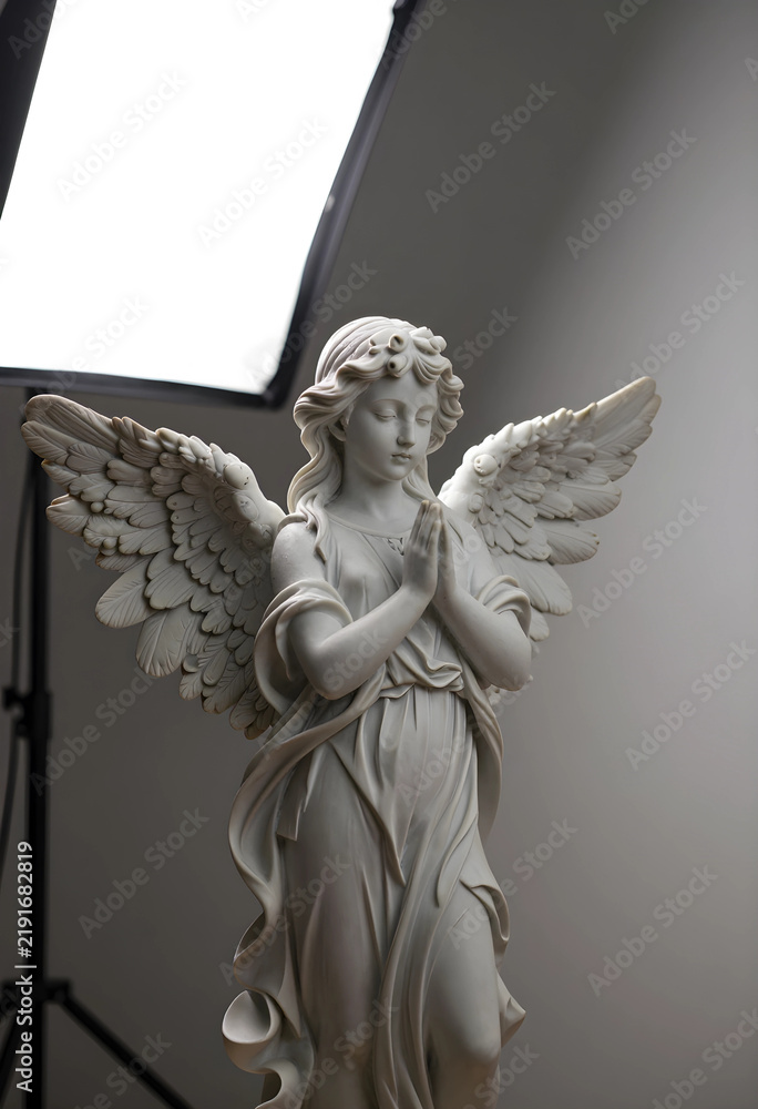 Fototapeta premium Spirituality and faith concept, marble angel statue with praying hands and wings in a studio setting for religious and memorial design projects