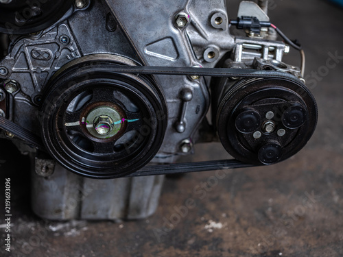 Close up of a car engine crankshaft pulley with serpentine belt connected to AC compressor