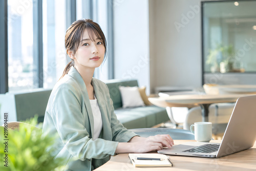 ビジネス オフィスでノートパソコン作業を中断して視線を向けるビジネスウーマン 自然光と広いコピースペースを生かした仕事風景