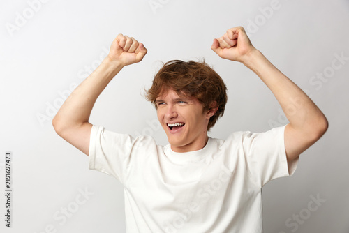 фотографія A man, excited, happy, smiling, raises arms in celebration, creating a moment of triumph and energy in a bright studio setting