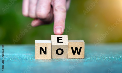 Ein Finger dreht den mittleren Buchstabenwürfel: Aus NOW wird NEW – Symbol für Veränderung, Innovation, Neustart und Zukunft.