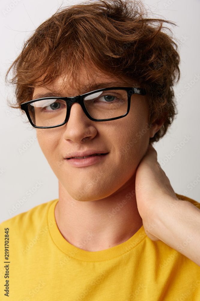 Fototapeta premium A young man wearing glasses and a yellow shirt, posed in a casual portrait with a warm smile, conveying approachable confidence.