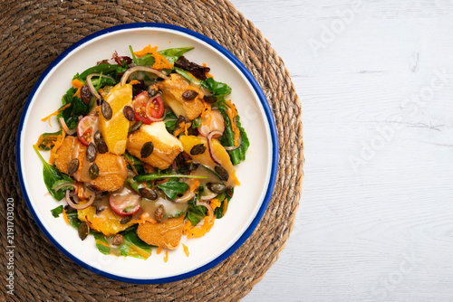 Overhead view of salad with fried cheese, orange slices, and pumpkin seeds. 