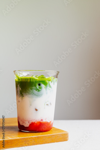Iced strawberry matcha latte in a glass on wooden board.