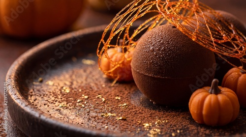 Gourmet Halloween chocolate dessert sphere decorated with spun sugar nest and miniature pumpkins on rustic plate dusted with cocoa powder and gold leaf