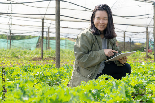 A young female farm owner uses a digital tablet to monitor and record crop growth on an organic vegetable farm.