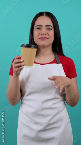 Young female hispanic barista showing a disgusting face while holding a paper cup of coffee