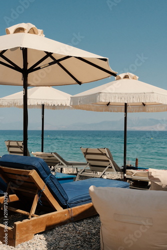 Fotografía Beach loungers and fringed umbrellas by turquoise sea, photographic style, clear