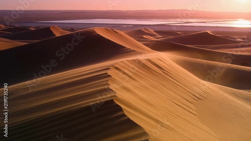 Light wind rising dune ridge casting drifting sand as low sun sculpting ripples over desert saltpan