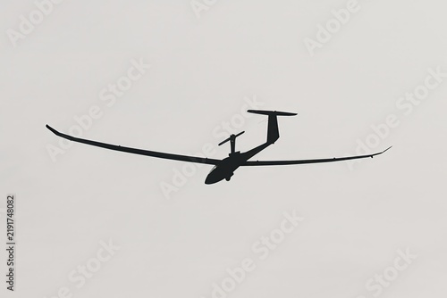 Motor glider silhouette taking off against a pale sky