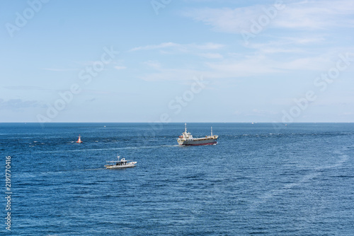 Small boat and cargo ship sail calm blue ocean water with distant horizon