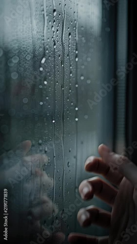 Extreme close-up shot of a human hand gently touching a rain-streaked window