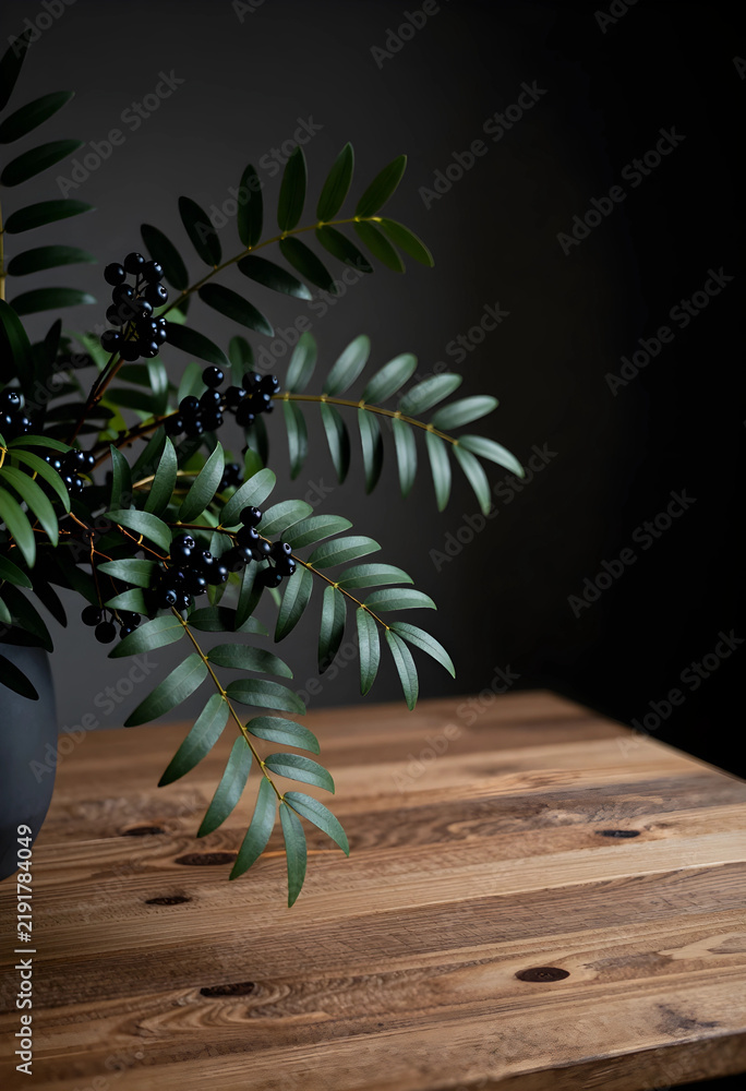 Obraz premium Minimalist interior decor, botanical arrangement with dark berries and green leaves on a rustic wooden table in a moody home office or living room space