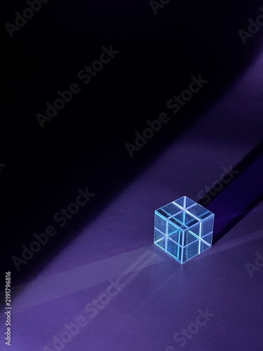 Transparent geometric cube illuminated by blue and purple light with dramatic diagonal shadows on a dark