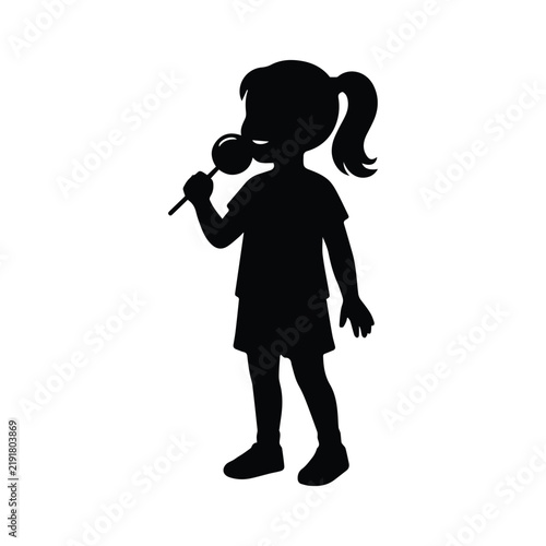 Silhouette of a young girl standing and eating a sweet lollipop on a stick for snack.