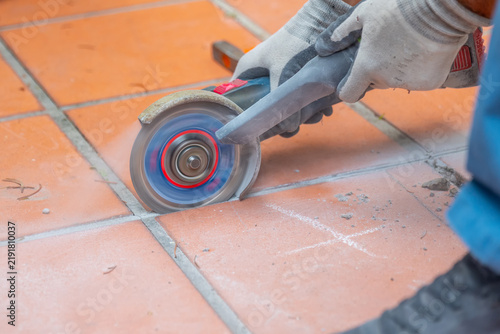 Worker wearing protective gloves cuts ceramic floor tiles with an electric angle grinder during renovation work.
