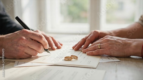 Couple signing legal documents with two gold wedding rings on table