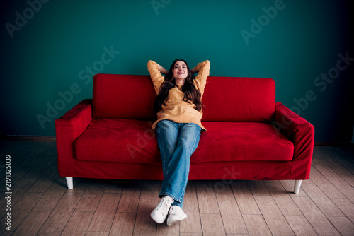 Bild auf Leinwand Young woman relaxing and smiling on a red sofa in a cozy living room, casual lif