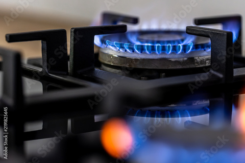 Gas stove burner with blue flame. Close view of black cooktop and metal grate.