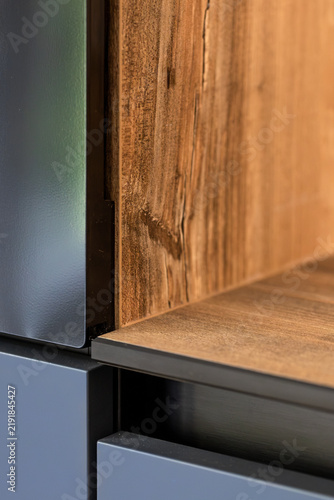 Wood grain shelf between dark cabinet panels. Contemporary interior joinery detail.