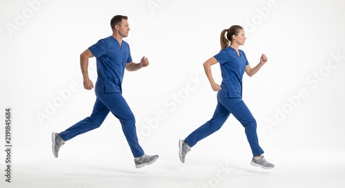 A side view of a young male and female doctor running in blue scrubs