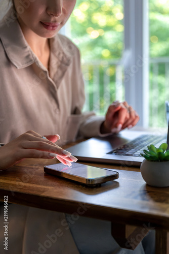 Woman tapping smartphone at home workspace. Remote work with laptop and mobile device.