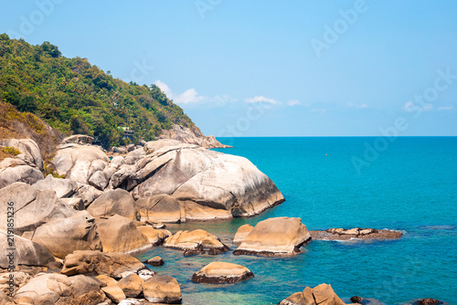 Bild auf Leinwand Large stone boulders line a rugged tropical coastline next to bright blue sea water on Koh Phangan
