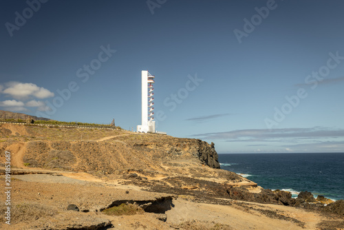 The modern white Buenavista Lighthouse stands tall on a rugged coastal cliff overlooking the vast expanse of the Atlantic Ocean in Tenerife, Spain.