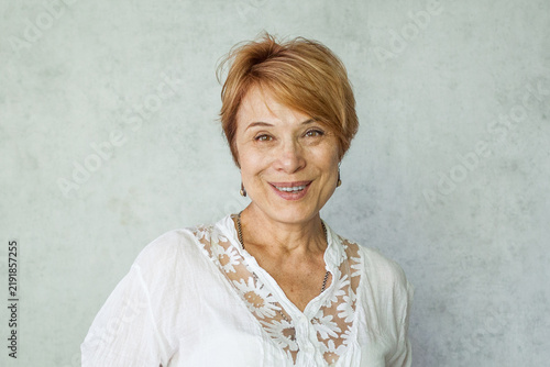 Joyful elegant senior woman wearing casual white shirt standing over grey background, happy face smiling. Positive person.
