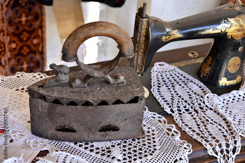 Tapety artystyczne Vintage Charcoal Flat Iron and Antique Sewing Machine on White Lace Doily