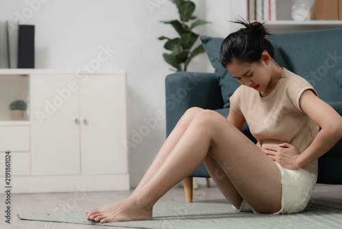 Abdominal pain concept showing a woman sitting on the floor and holding her lower stomach in discomfort at home. abdominal pain, woman, cramps, stomach, pelvic, healthcare, home