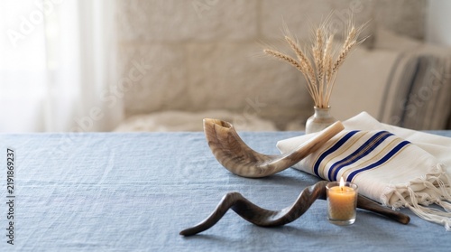 A shofar, a traditional Jewish ritual horn, sits beside a lit candle and a ceremonial cloth, evoking a sense of spiritual solemnity and reflection in a serene setting.