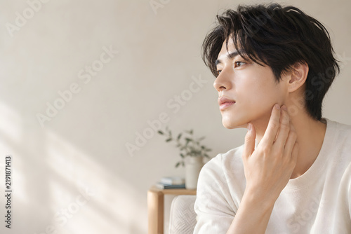 美容広告向け 顎に手を添え横顔で余白を見つめる男性 透明感のある肌と柔らかな自然光が映えるスキンケアイメージ