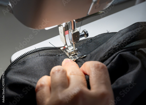 Sewing a zipper onto a black fabric bag with a sewing machine in an indoor workshop