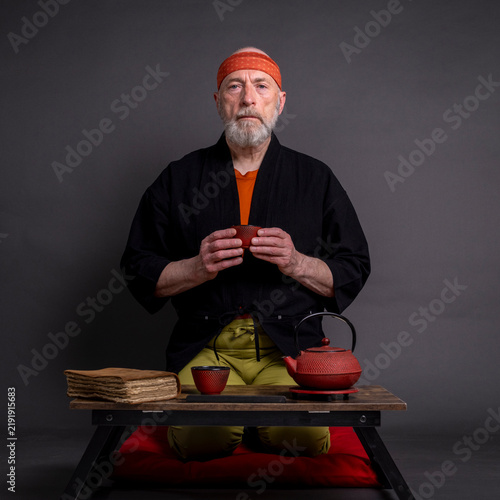 Tapety artystyczne portrait of senior man wearing a short kimono and sitting in a traditional Japanese seiza position on a cushion pad, and drinking tea